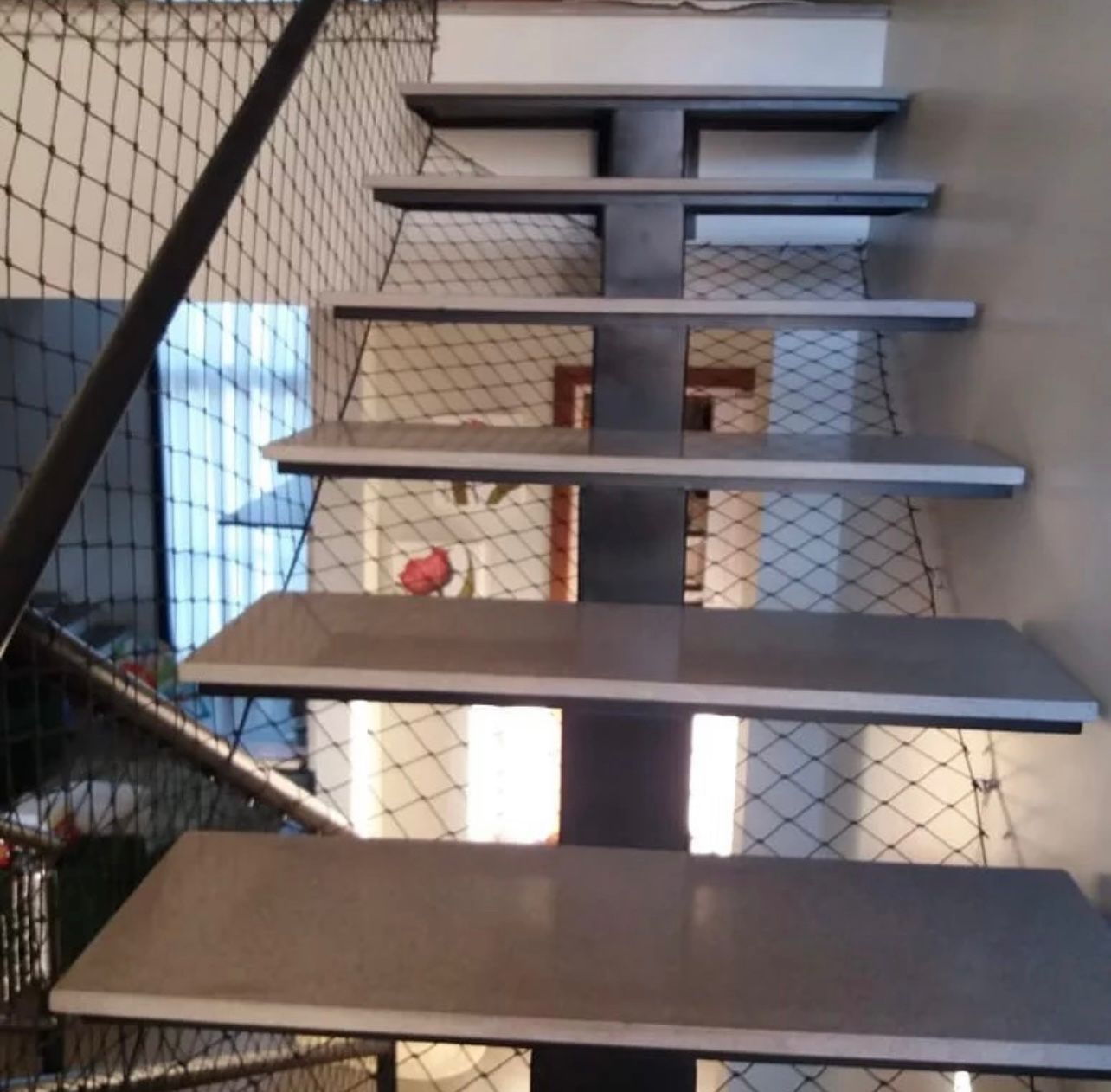 Escada vazada com rede de proteção preta entre os degraus