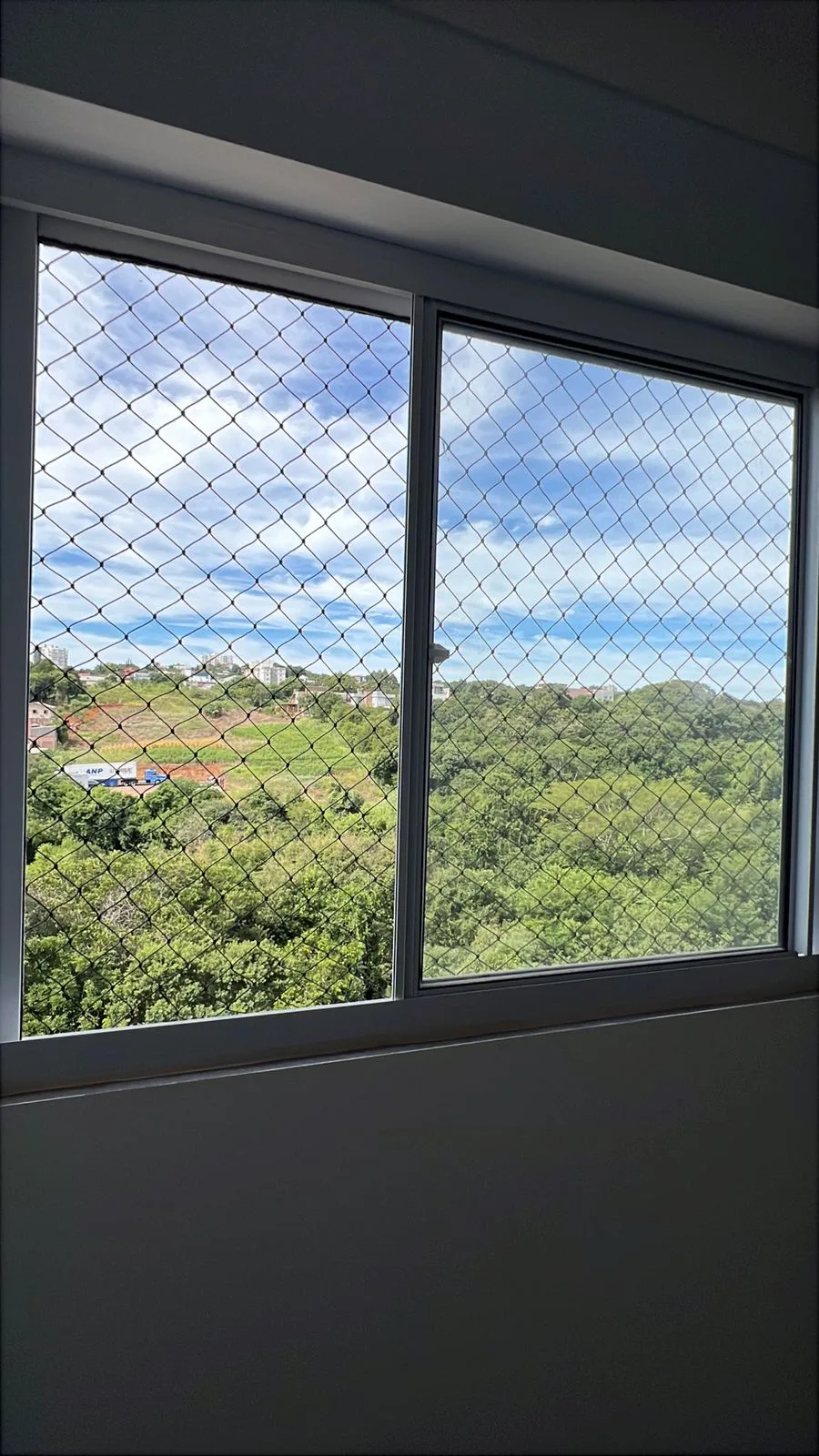 Janela com rede de proteção e vista para a natureza