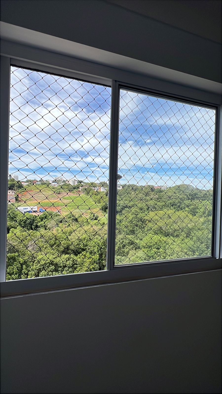 Janela com rede de proteção e vista para a natureza